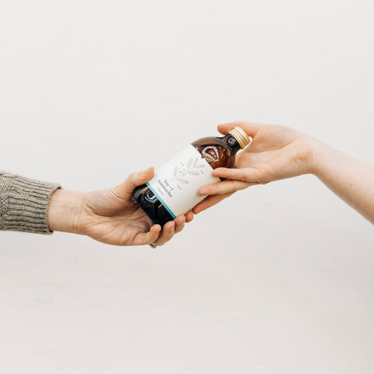 One hand passing a bottle of You + I kombucha to another