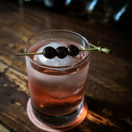 Cherry drink over ice in a rocks glass with a skewer of dark cherries