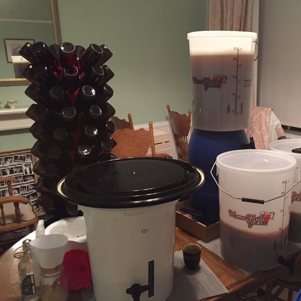 Early home brewing setup with fermentation buckets and a bottle drying rack