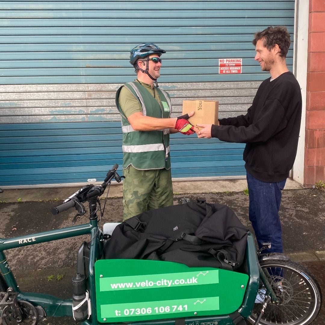 A Velo City cargo bike rider handing a You + I box over outside the Glasgow brewery