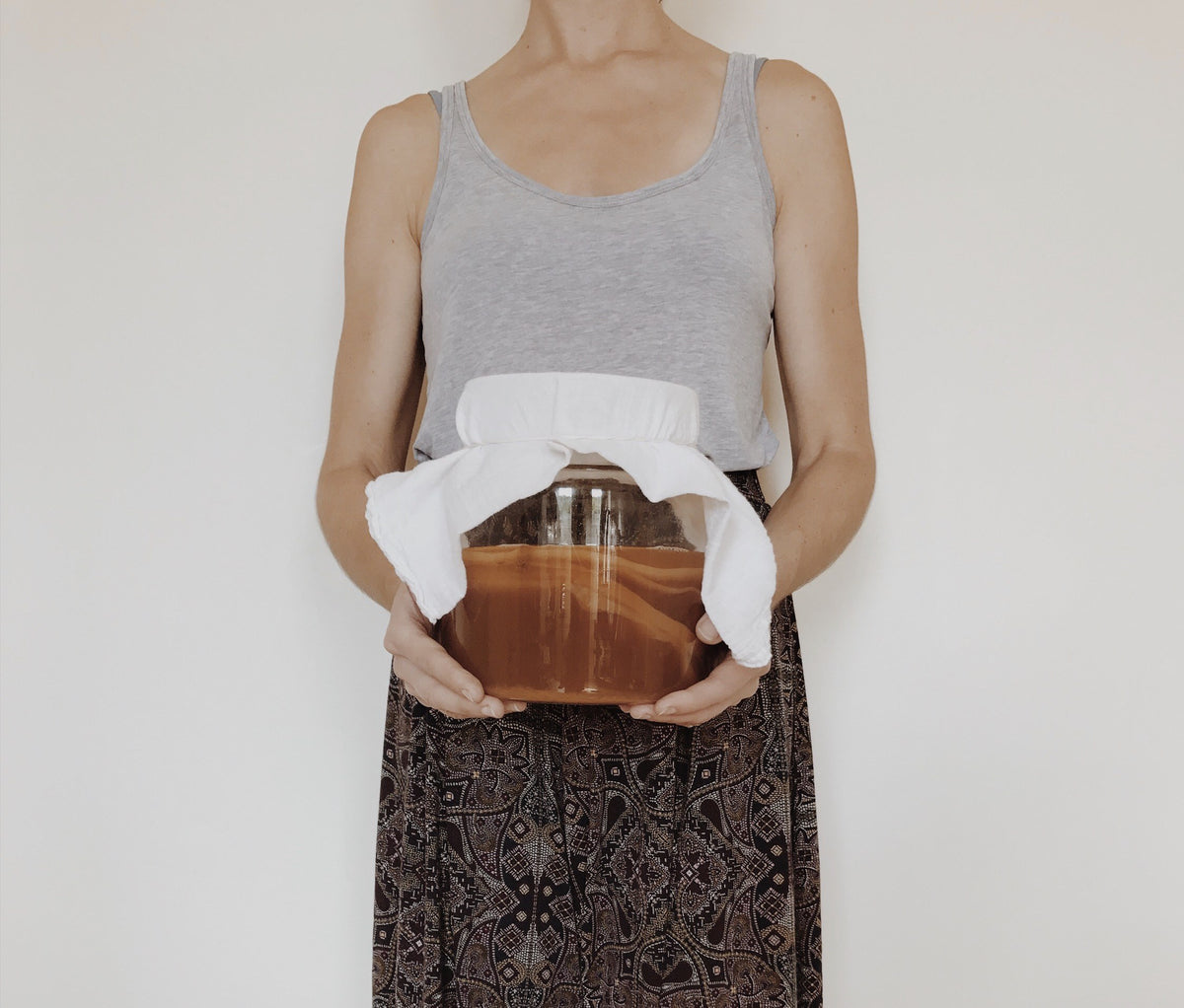 Holding a glass jar of kombucha fermenting under a cloth cover