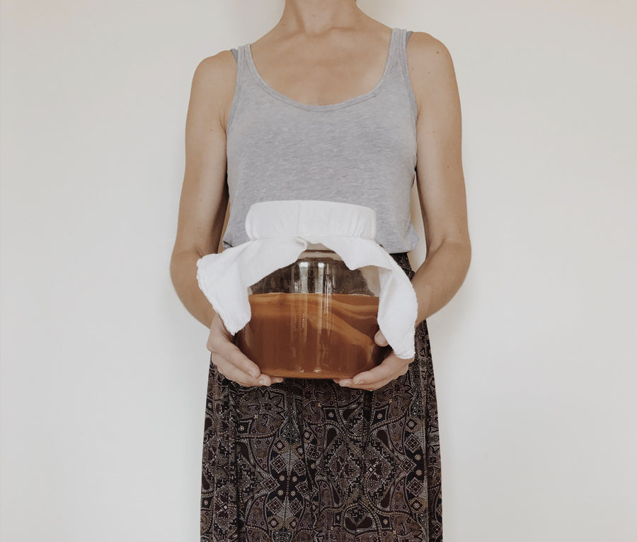 Holding a glass jar of kombucha fermenting under a cloth cover