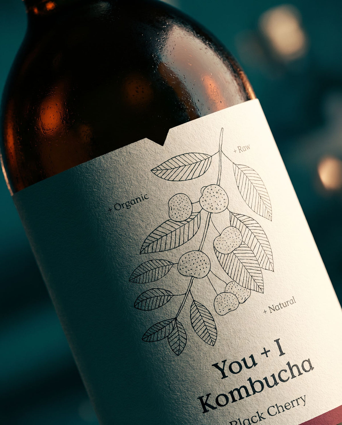 Close-up of a You + I Black Cherry kombucha bottle, its label marked raw, organic and natural
